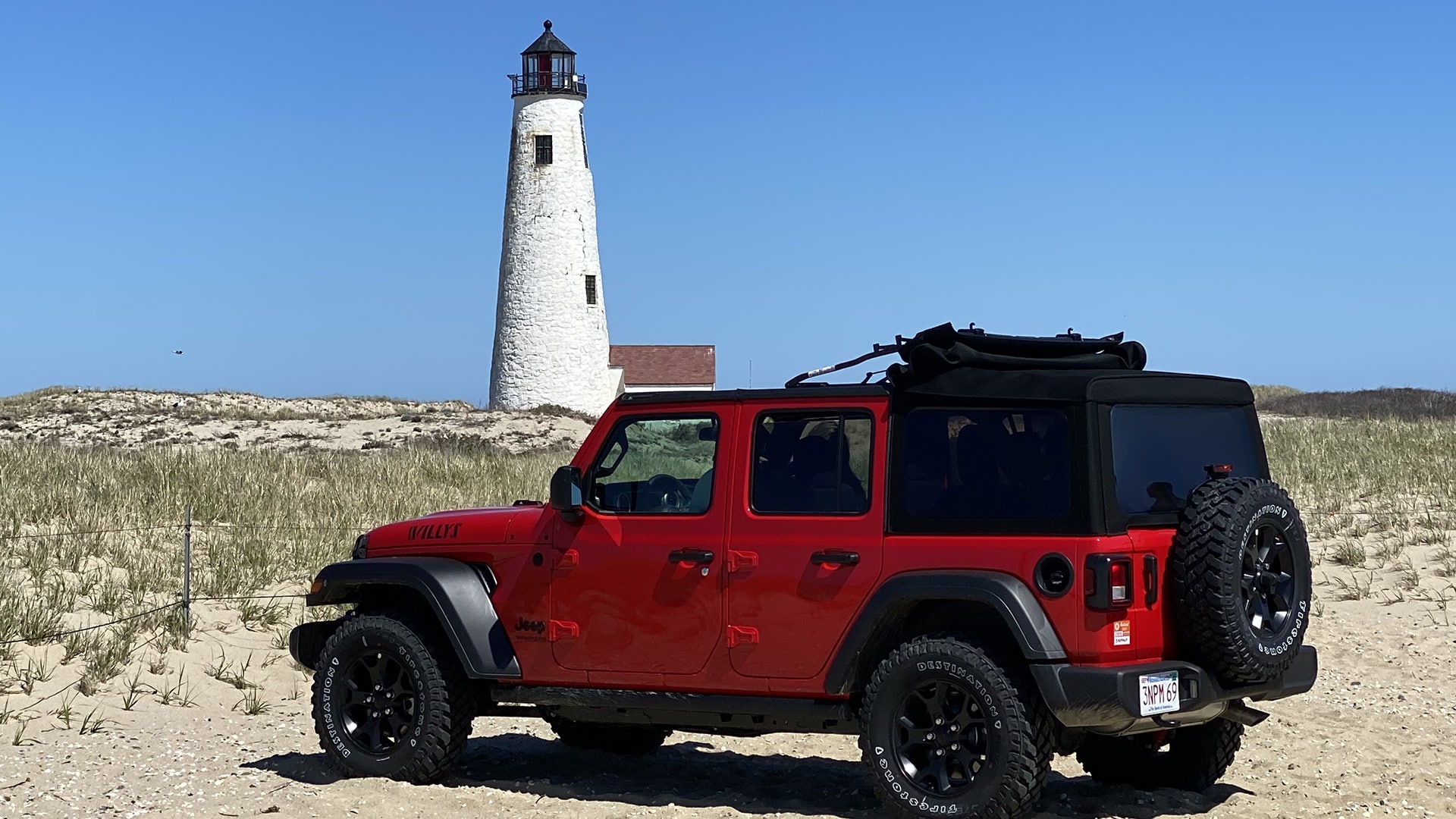 a red car in front of a white lighthouse on the beach