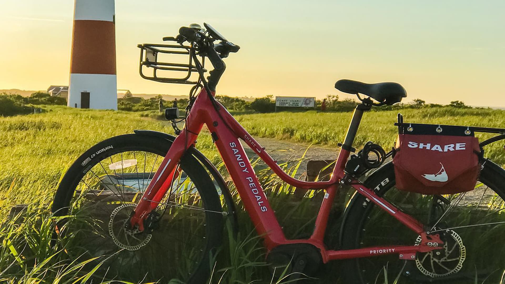 a red bike in a field with a red and white lighthouse in the background