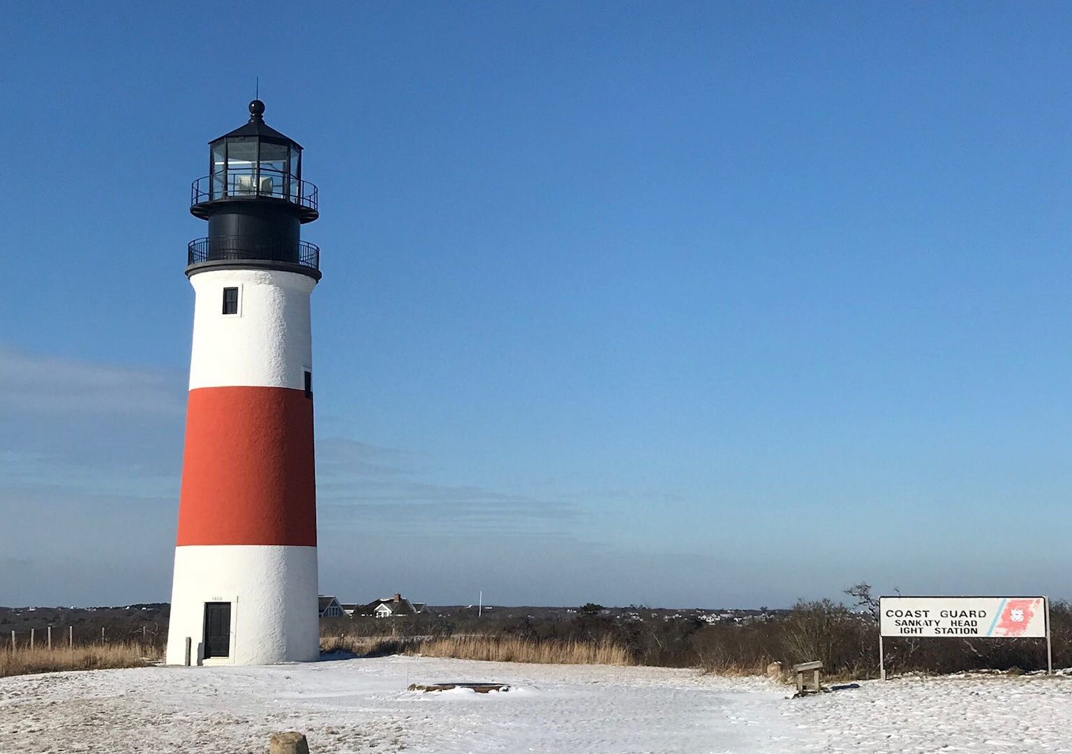 a white and red lighthouse a snow on the ground with blue sky