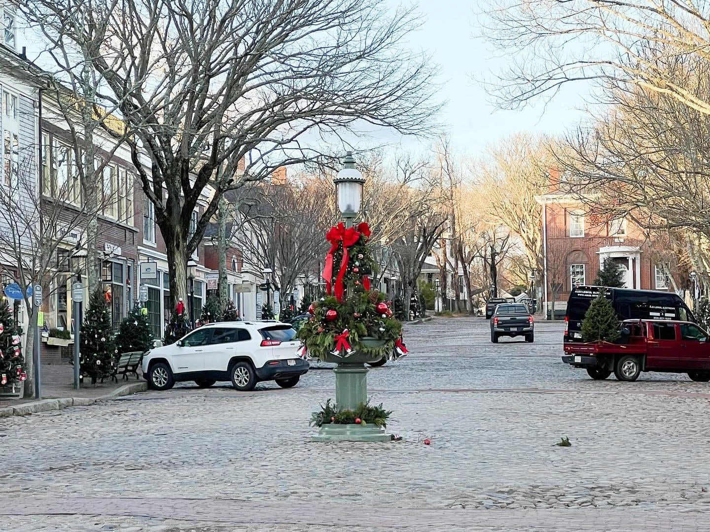 a christmas decorated light on a cobblestone road and cars