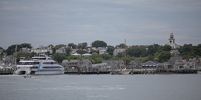a boat in the harbor with a village in the background with a church steeple