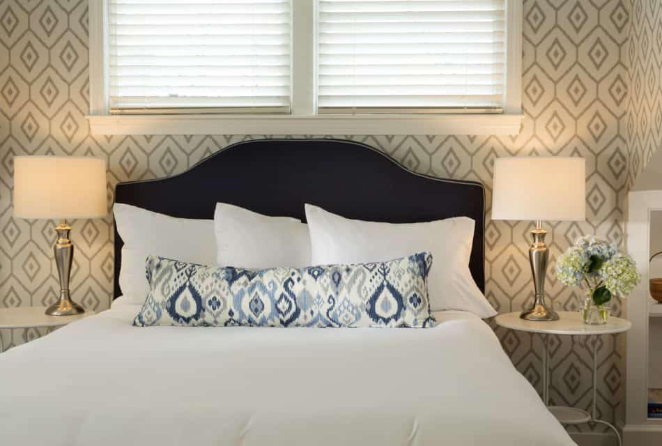 Bedroom with wooden flooring, light colored walls, navy upholstered headboard, white bedding, chrome lamps