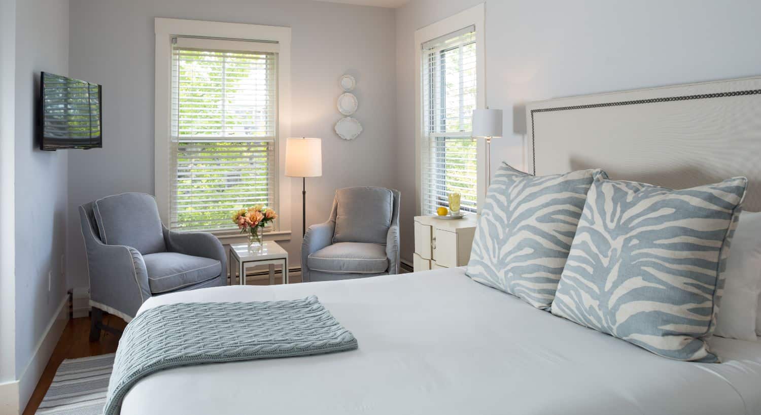 Bedroom with wooden flooring, light blue walls, white bedding, and two light blue upholstered chairs