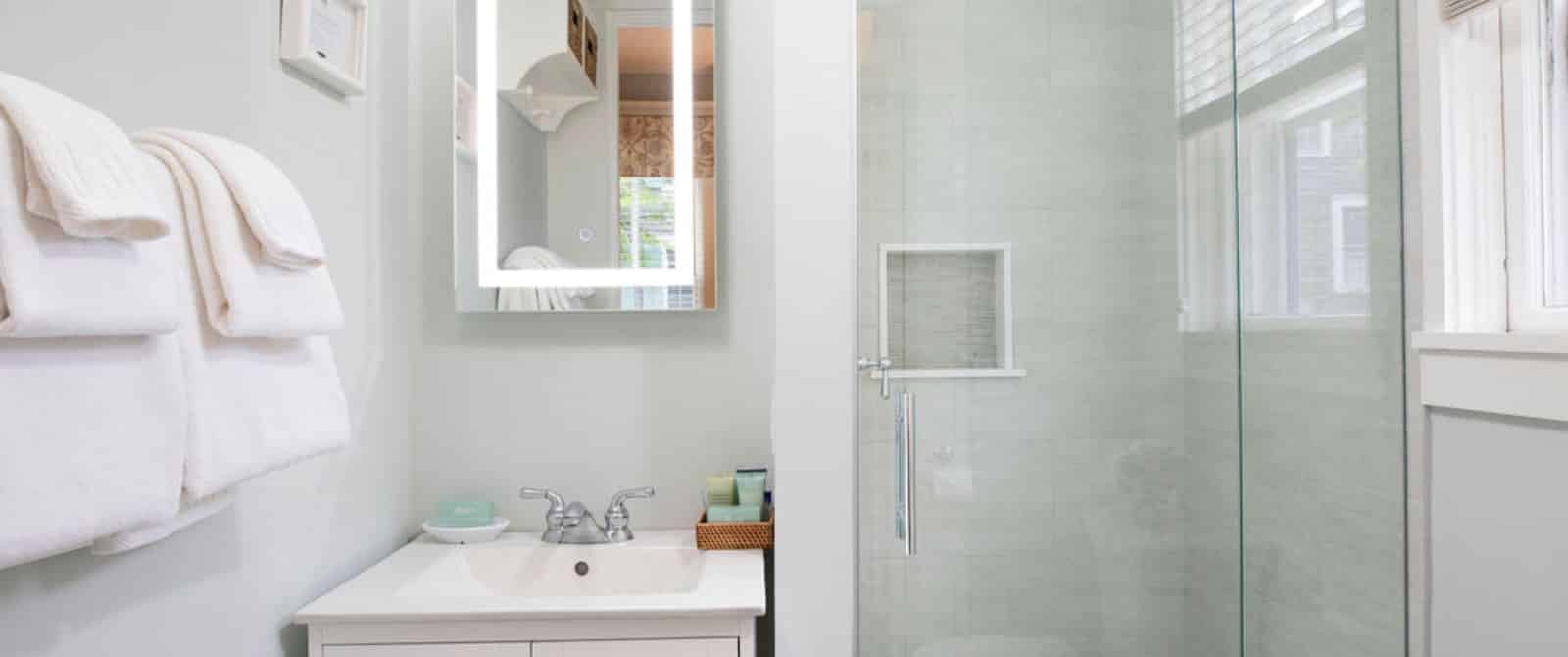 Bathroom with white walls, white vanity, rectangular mirror, and stand up shower
