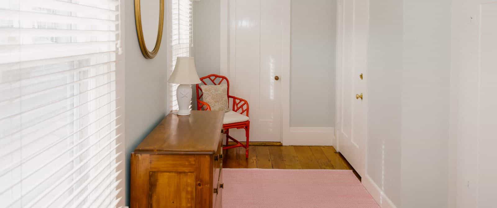 Hallway with light green walls, white trim, wooden flooring, dark wooden dresser, and orange chair