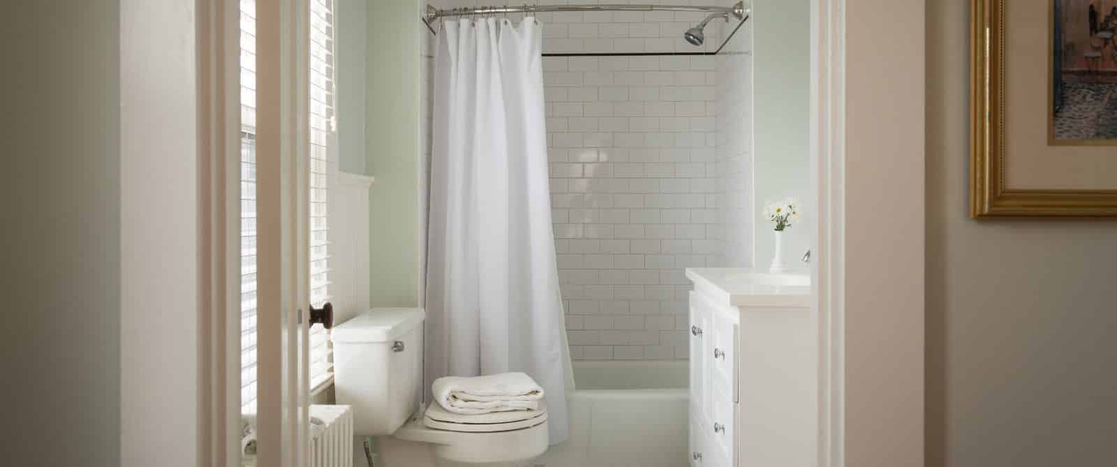 Bathroom with light green walls, white toilet, white dresser, white tub, white curtain, and white tile