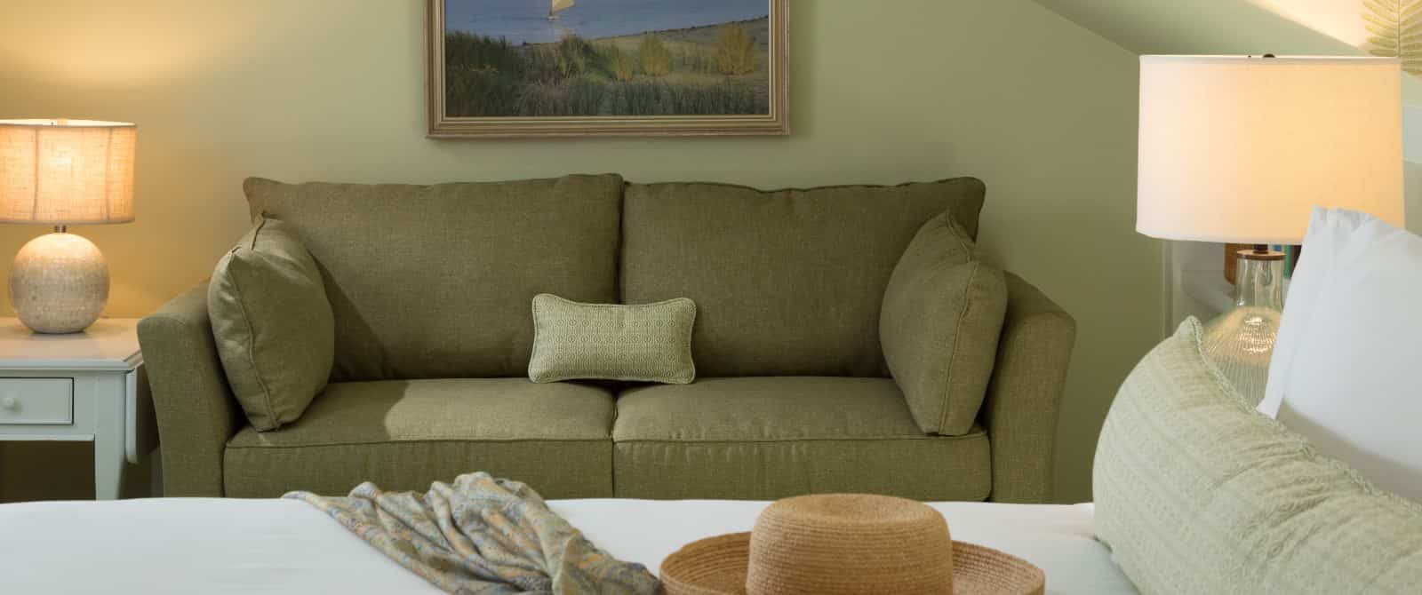 Bedroom sitting area with light green upholstered loveseat and white end table