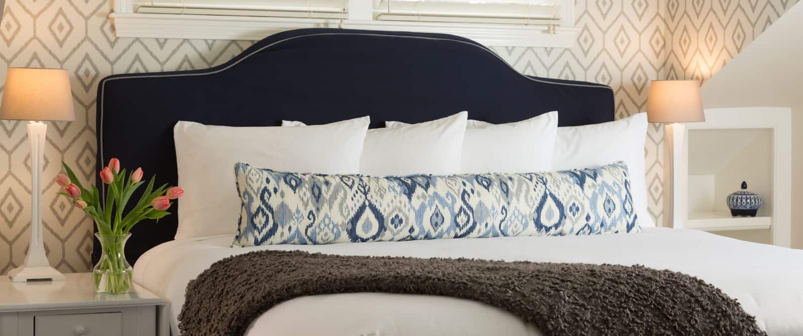 Bedroom with navy upholstered headboard, white bedding, and long pillow with hues of blue