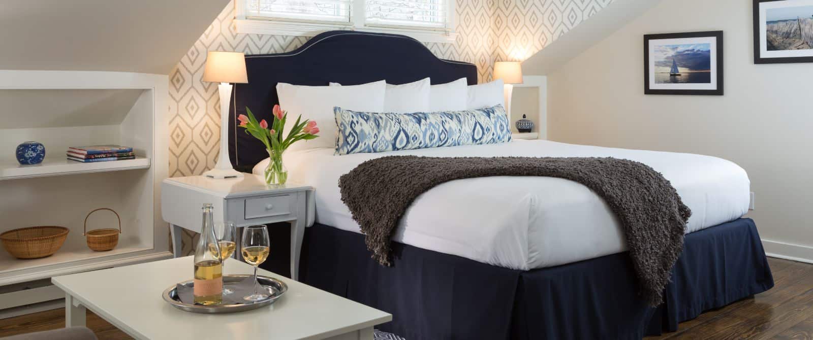 Bedroom with wooden flooring, light colored walls, navy upholstered headboard, white bedding, and sitting area