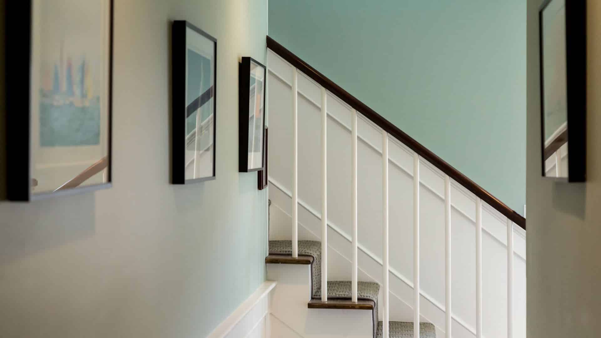 Hallway with mint green walls, white paneling, dark wooden stairs, and pictures hanging on the walls