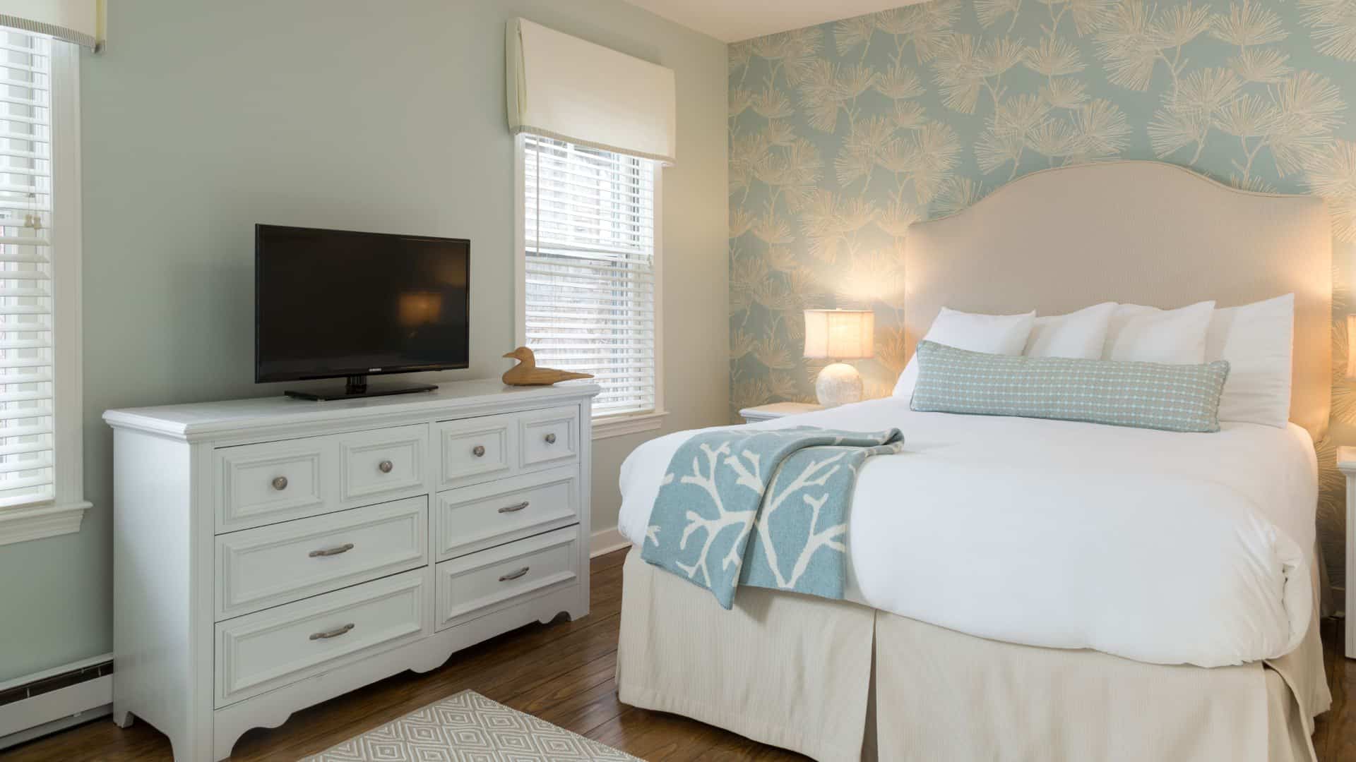 Bedroom with wooden flooring, light green walls, cream upholstered headboard, white bedding, and white dresser