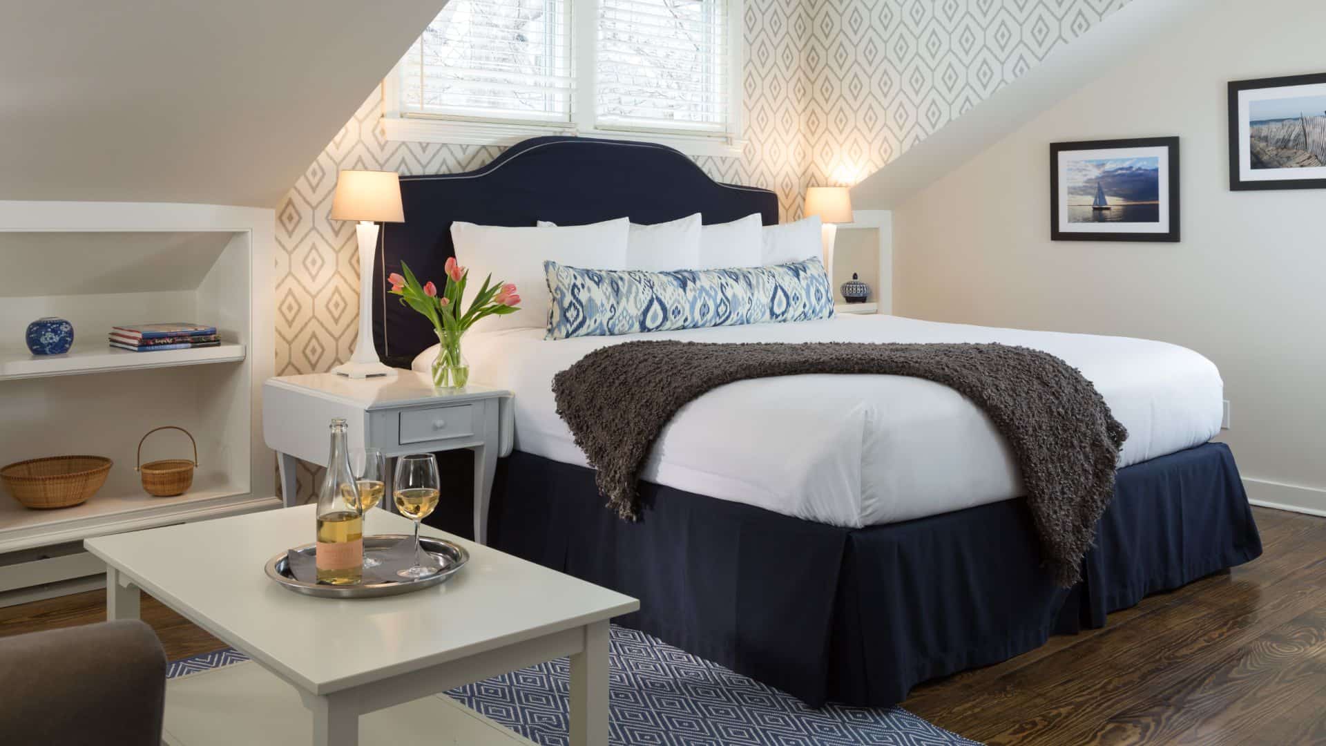 Bedroom with wooden flooring, light colored walls, navy upholstered headboard, white bedding, and sitting area