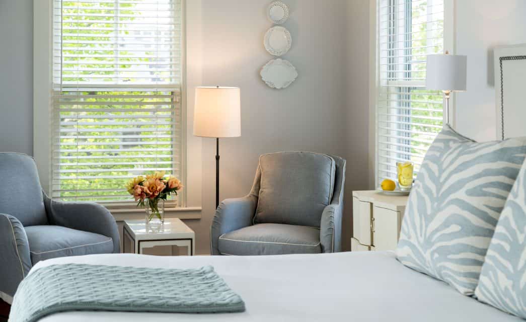 Bedroom with light blue bedding, white bedroom furniture, and blue upholstered chairs in sitting area