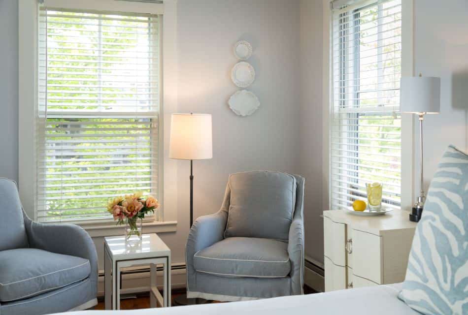 Bedroom with wooden flooring, light colored walls, white bedding, and two light blue upholstered chairs