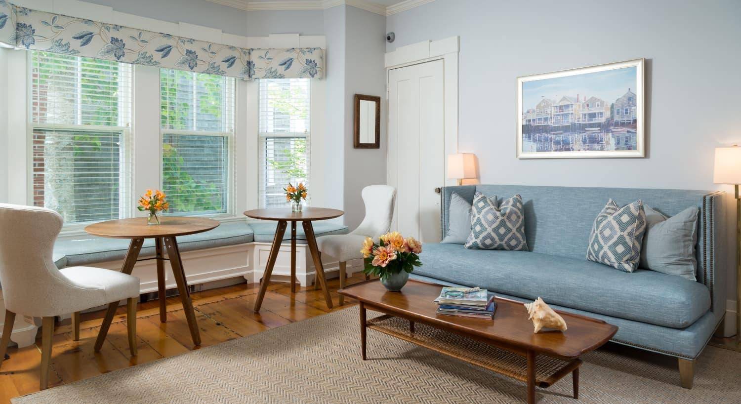 Living room area with hardwood flooring, light colored walls, white trim, blue upholstered couch, and wooden furniture
