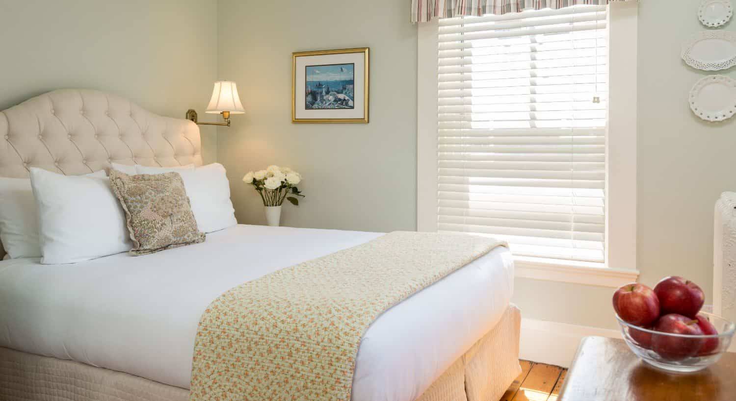 Bedroom with wooden flooring, light green walls, cream upholstered headboard, white bedding, and dark wooden dresser